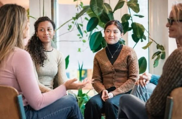 Grupo de mulheres sentadas em círculo a conversar, numa sala com plantas